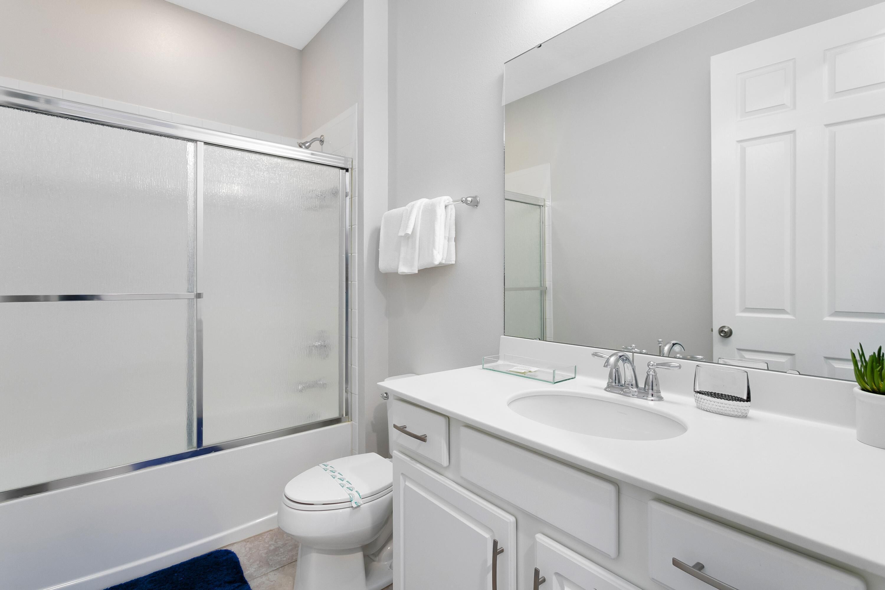 A modern bathroom with a glass shower enclosure, a white toilet, a sink with a mirror, and a potted plant.
