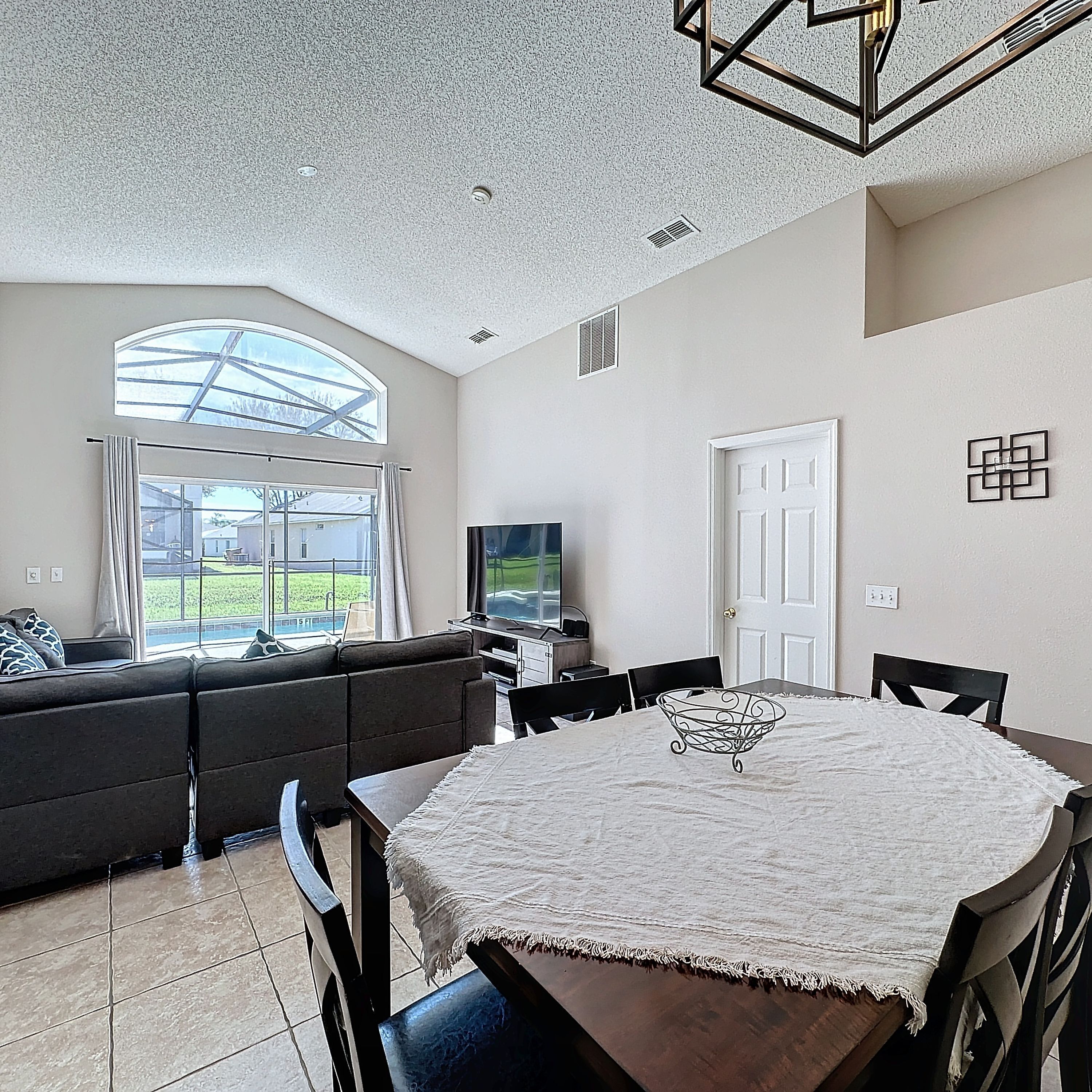 A modern living room with a large window, a dining area with a round table, and a built-in entertainment unit.
