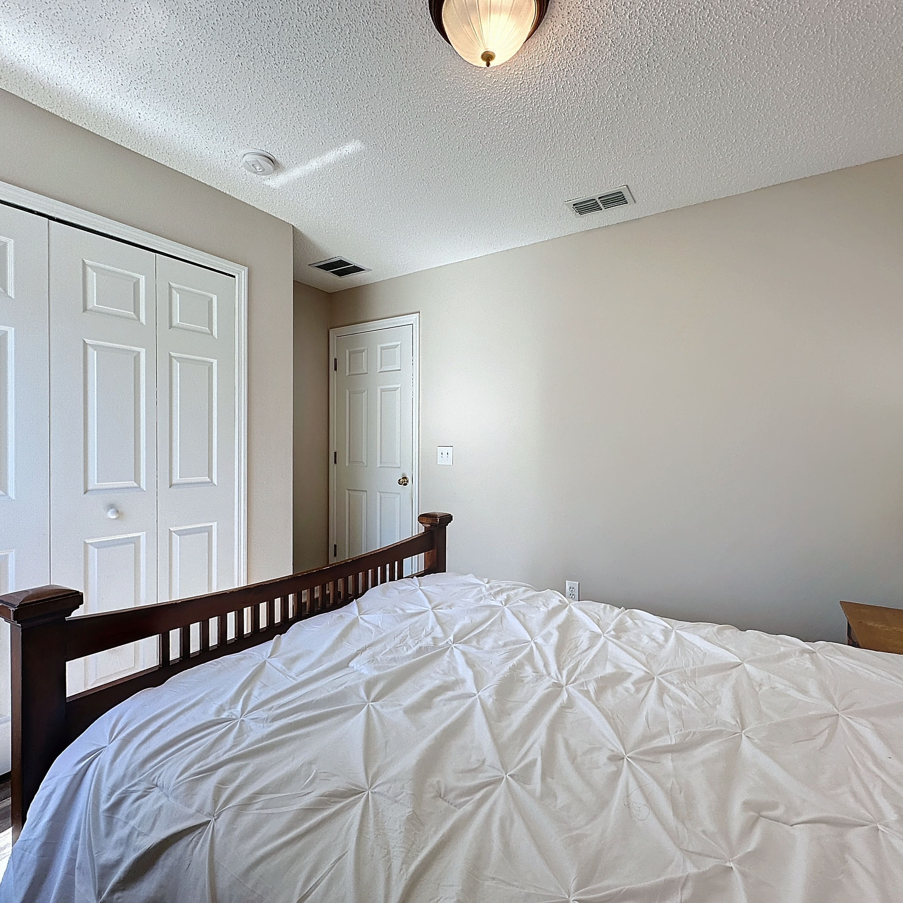 A bedroom with a bed, a wooden headboard, a white door, and a light fixture on the ceiling.