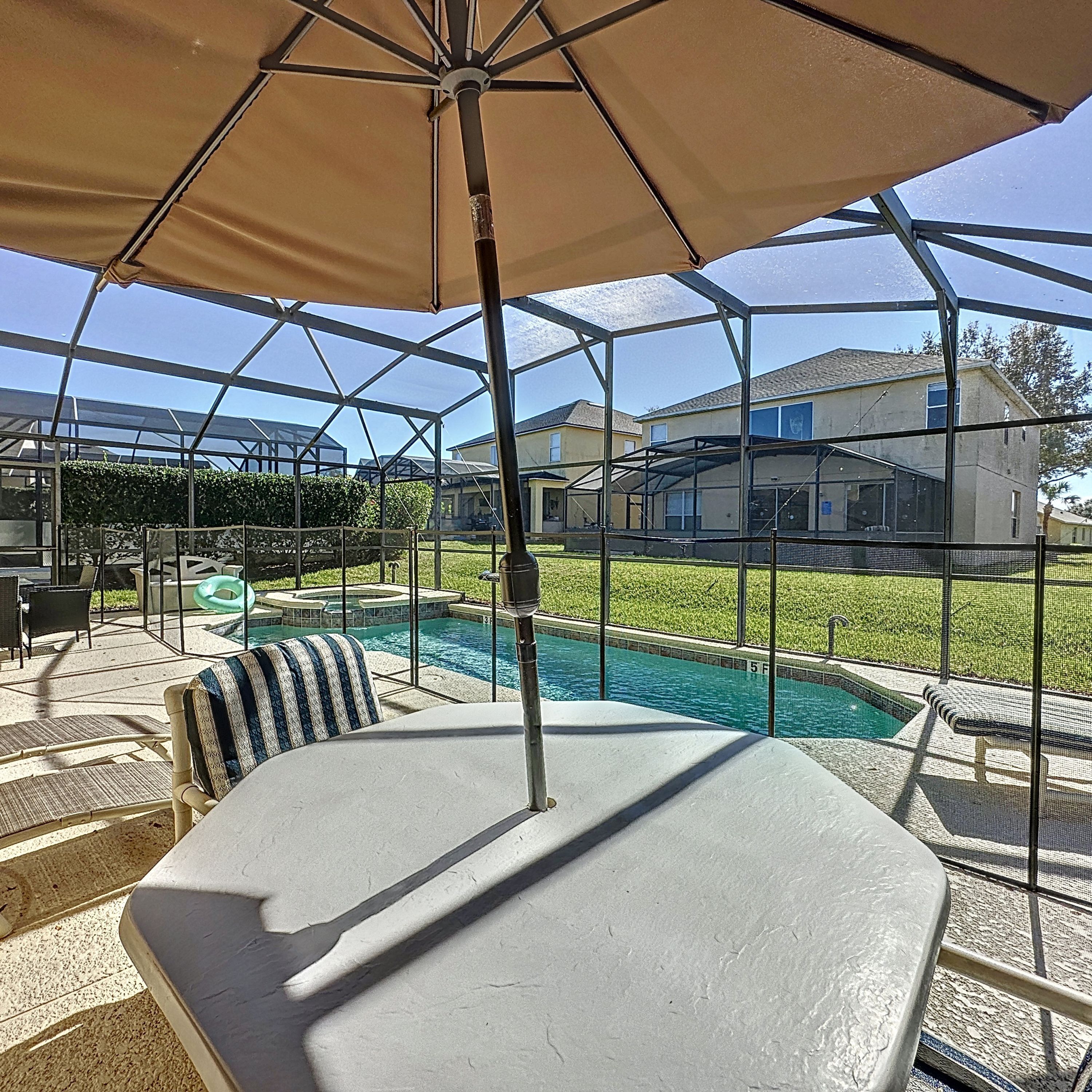 A covered outdoor area with a pool, lounge chairs, and a table.