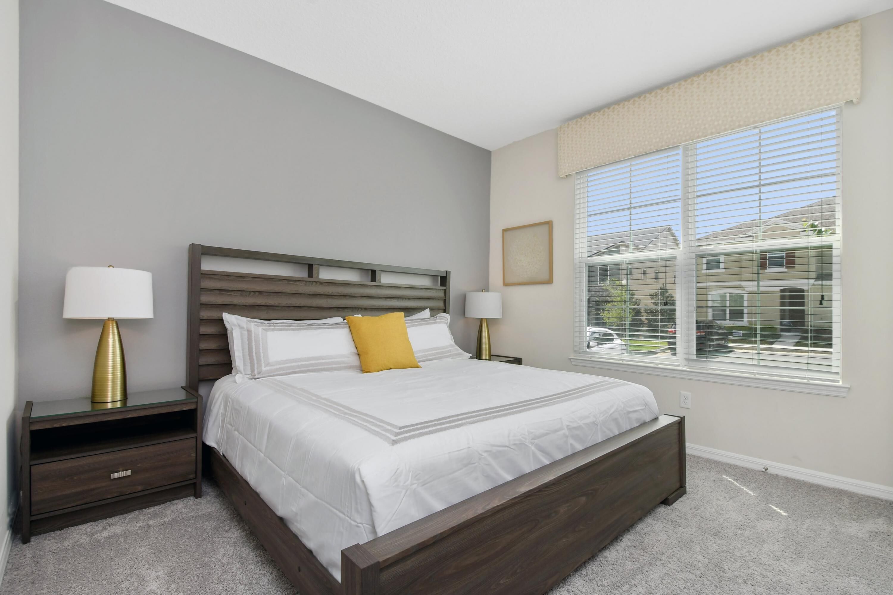 Une chambre à coucher avec un grand lit, deux tables de chevet, une fenêtre avec des stores et une vue sur l’extérieur.