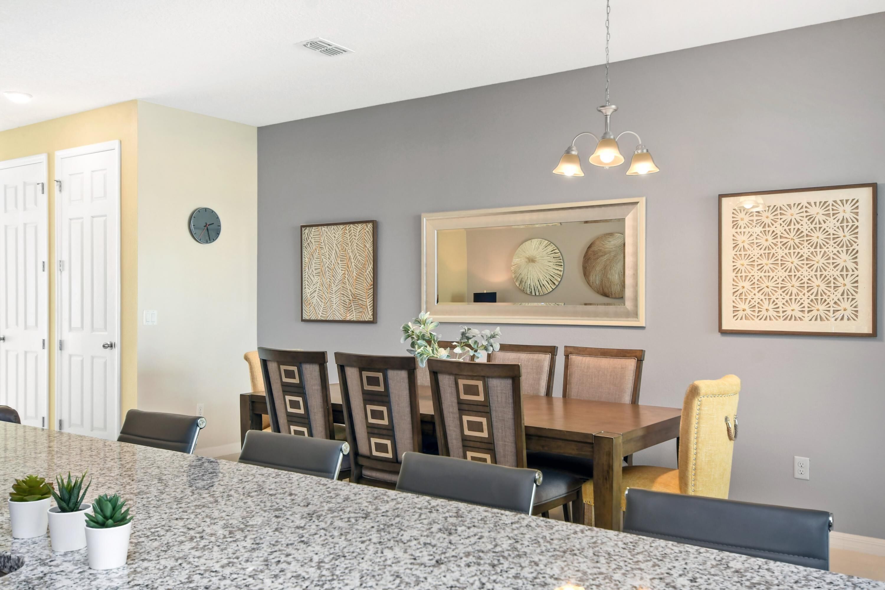 A dining area with a granite table, wooden chairs, and a chandelier.