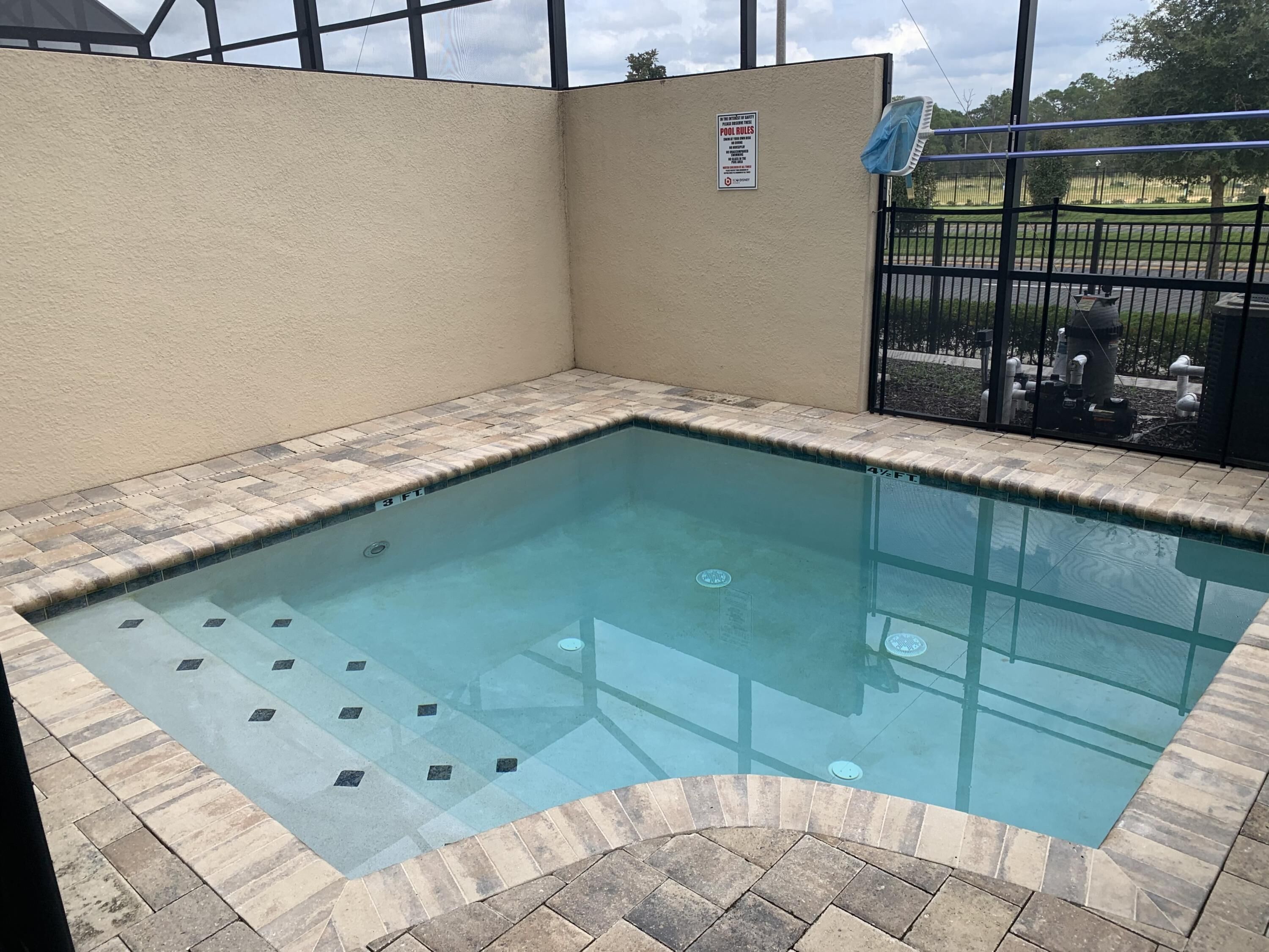 A small, rectangular indoor pool with a tiled edge and a sign indicating pool rules.