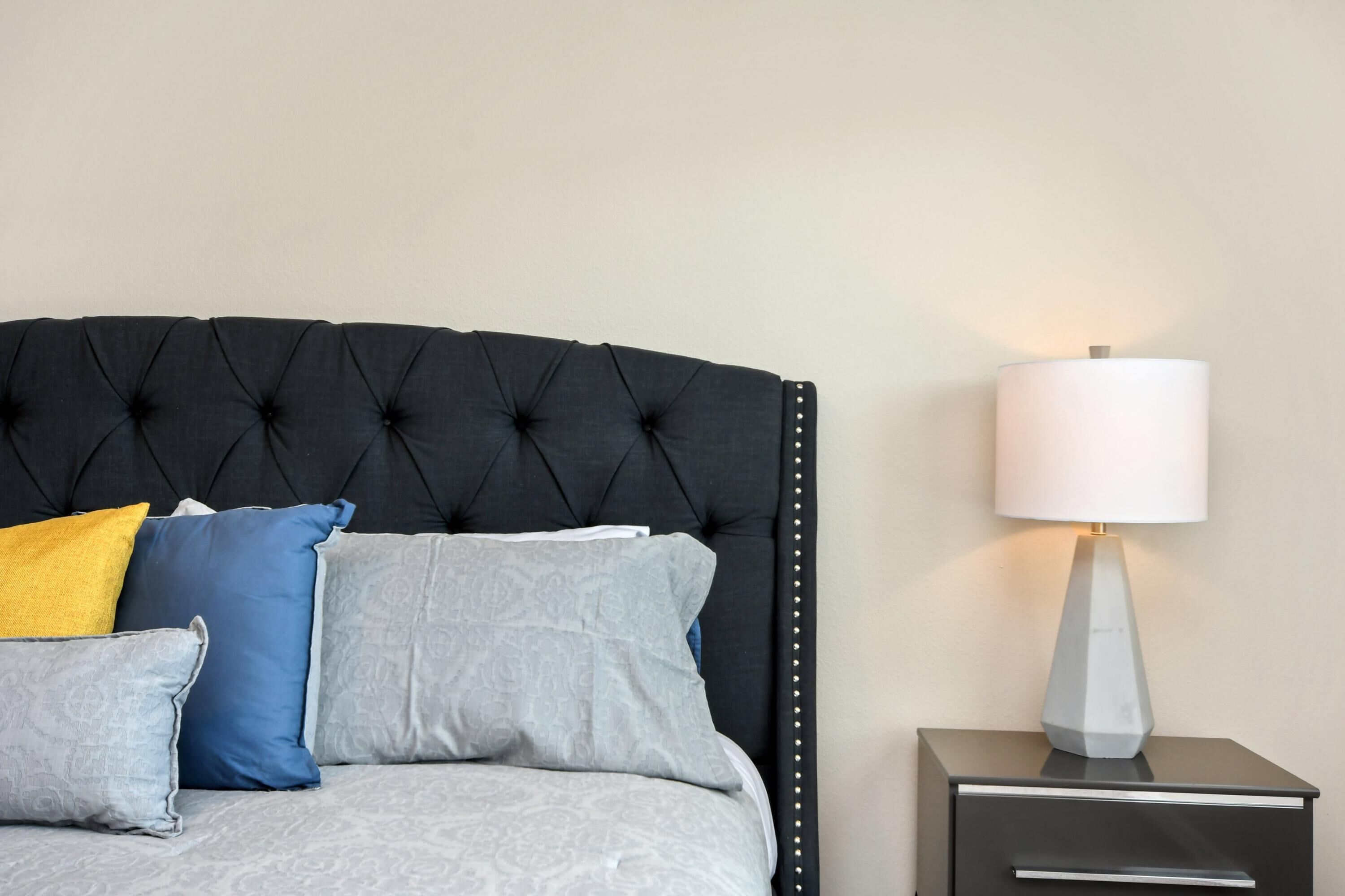 A bed with a tufted headboard, a bedside table with a lamp, and multiple pillows.