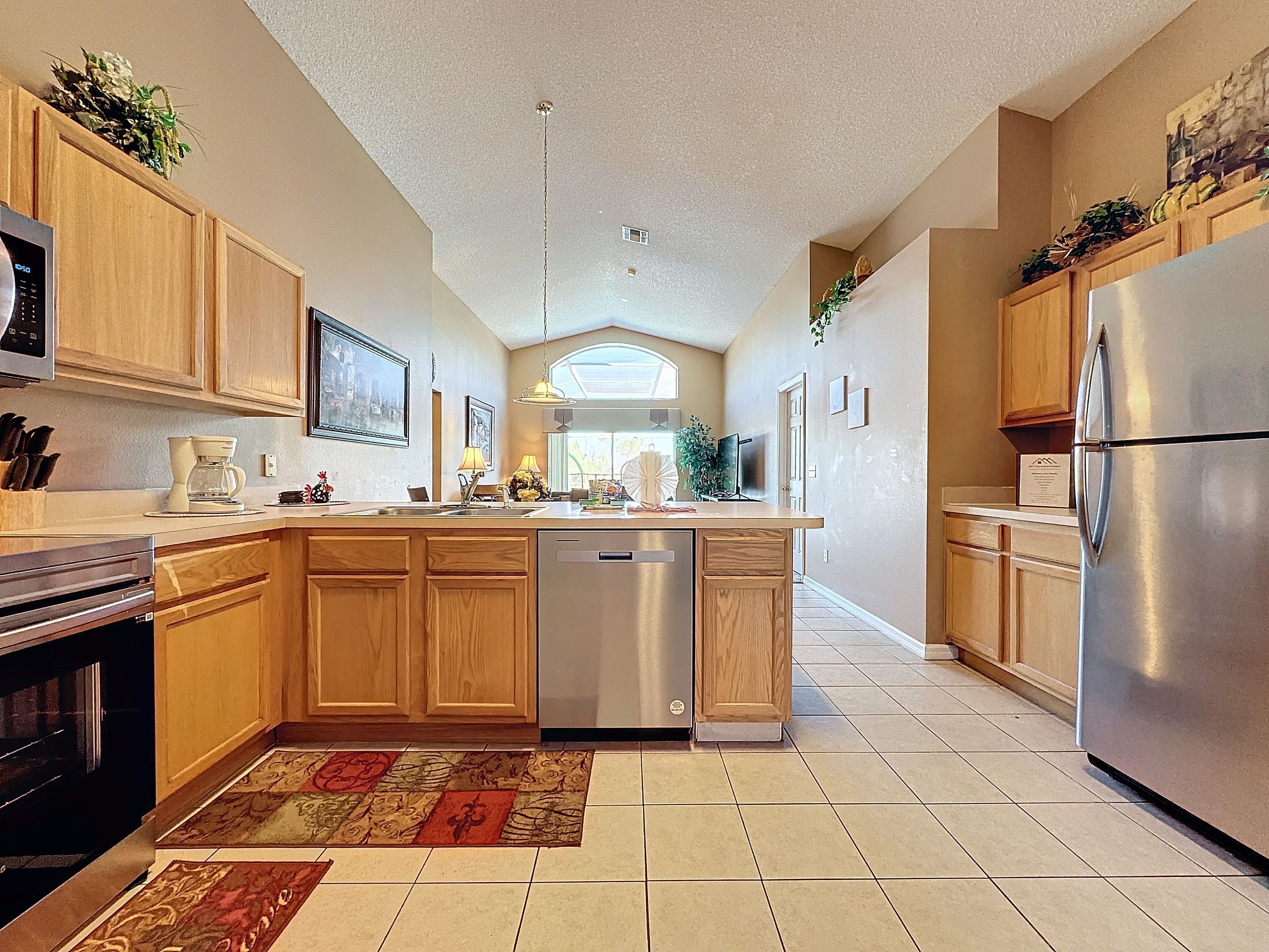 A kitchen with wooden cabinets, a stainless steel refrigerator, a dishwasher, and a tiled floor.