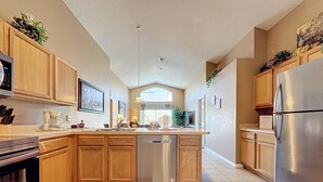 A modern kitchen with wooden cabinets, a stainless steel refrigerator, a dishwasher, and a coffee maker.