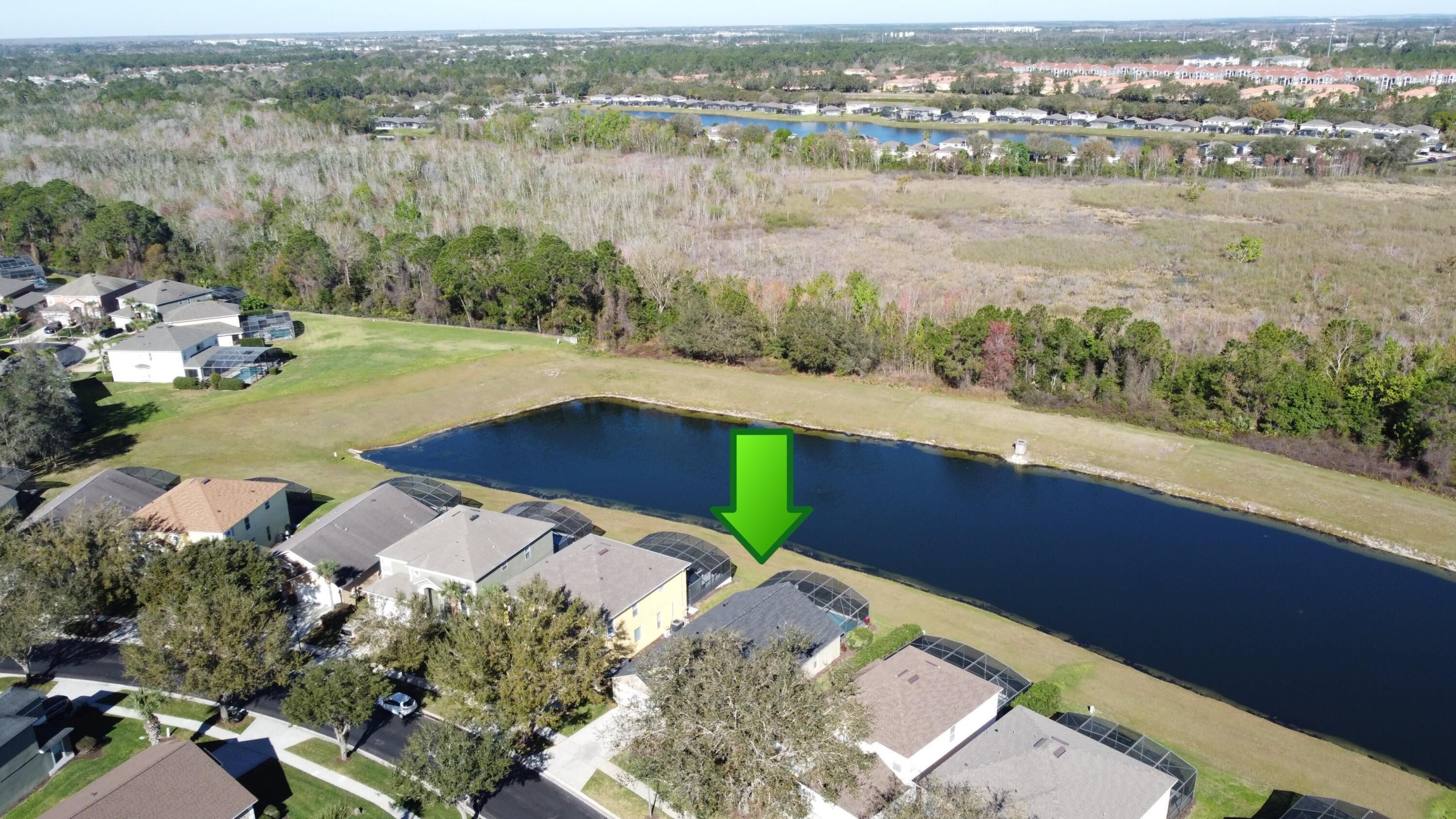 An aerial view of a residential area with houses, a large pond, and a green arrow pointing to the pond.
