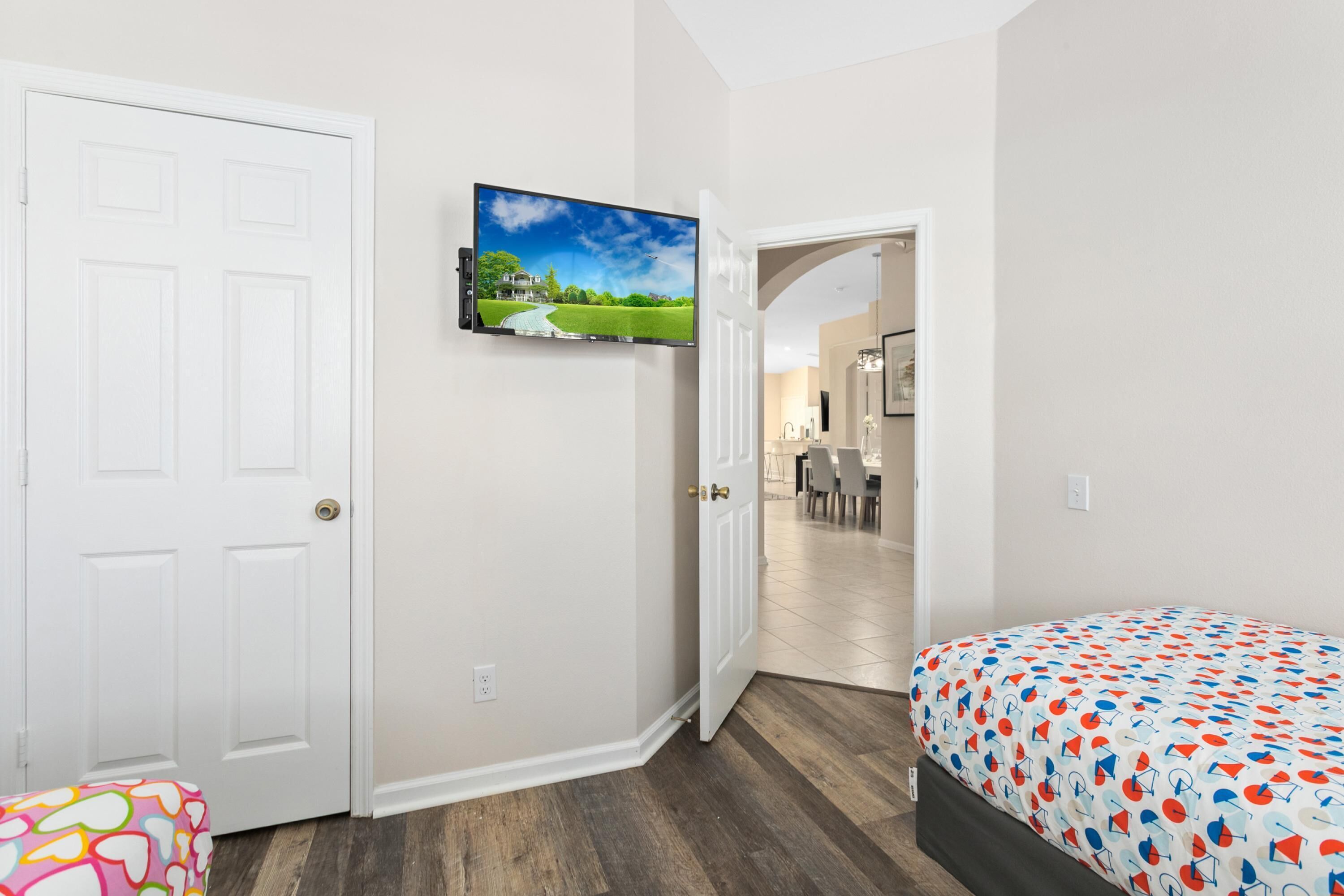 A bedroom with a bed, a TV mounted on the wall, and a door leading to another room.