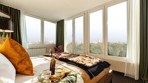 A hotel room with a large bed, a city view, a window with curtains, and a tray with cups and a vase. - Qult·co - The Renaissance Affair (București)