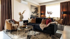 A modern living room with a dark sofa, armchairs, a coffee table, and a painting on the wall. - Qult·co - The Aristocrat (București)