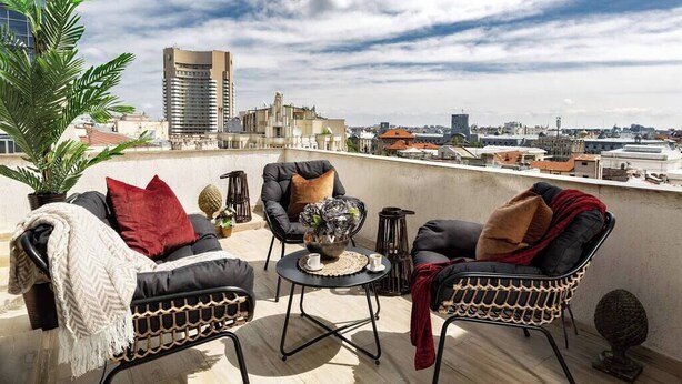A rooftop terrace with outdoor furniture, a view of the cityscape, and a tall building in the background. - Qult·co - The Aristocrat (București)