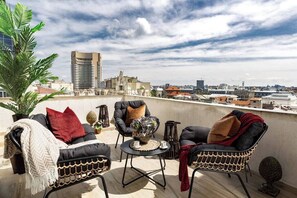A rooftop terrace with outdoor furniture, a view of the cityscape, and a tall building in the background.
