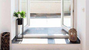 A room with a wooden floor, a potted plant, a wicker basket, and a view of a cityscape through open sliding doors.