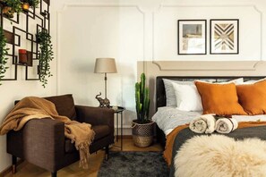 A modern bedroom with a bed, a sofa, a lamp, a cactus, and a wall with geometric decor.