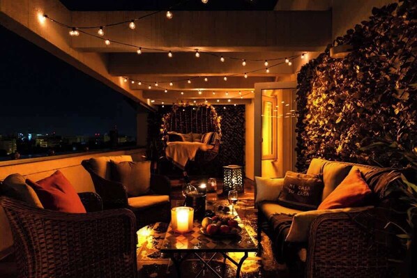 A rooftop terrace with wicker furniture, string lights, and a candle.