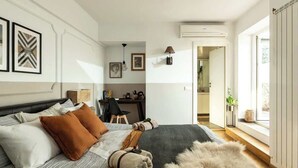 A bedroom with a bed, pillows, a desk, and a window.