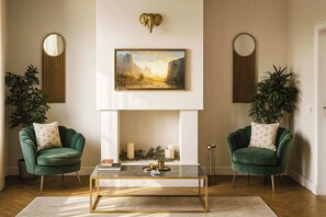 Ein Wohnzimmer mit zwei grünen Sesseln, einem Couchtisch, einem Kamin und einem darüber hängenden Gemälde.