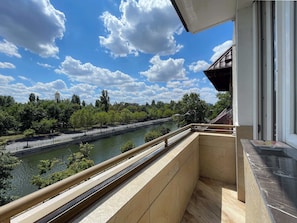 Ein Balkon mit Blick auf einen Fluss, Bäume und ein Gebäude in der Ferne.
