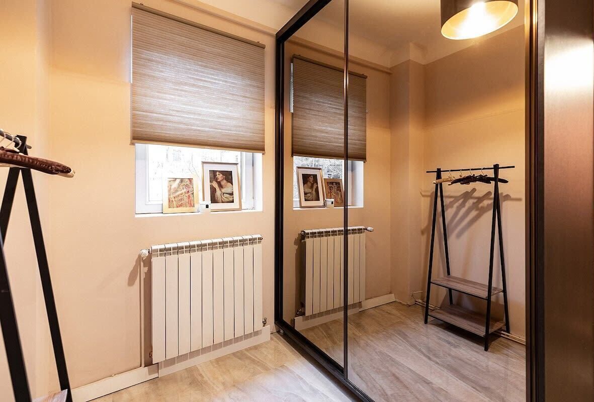 Een kamer met een radiator, een raam met jaloezieën, een spiegel en een plank met spullen.