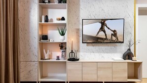 Un salon moderne avec un mur en marbre, un téléviseur fixé au mur, un meuble en bois et une étagère ornée d’objets décoratifs.