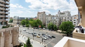 Un immeuble à plusieurs étages doté de balcons, une rue animée où circulent des voitures et un ciel dégagé.