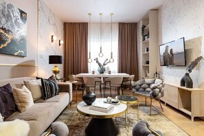 A modern living room with a sofa, coffee table, dining table, and a TV.