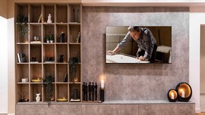 Un salon moderne doté d’un téléviseur encastré, d’étagères en bois ornées d’objets décoratifs et d’une cheminée avec des bougies.