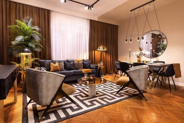 A modern living room with a sofa, two armchairs, a coffee table, a dining table with chairs, a large mirror, and a potted plant.