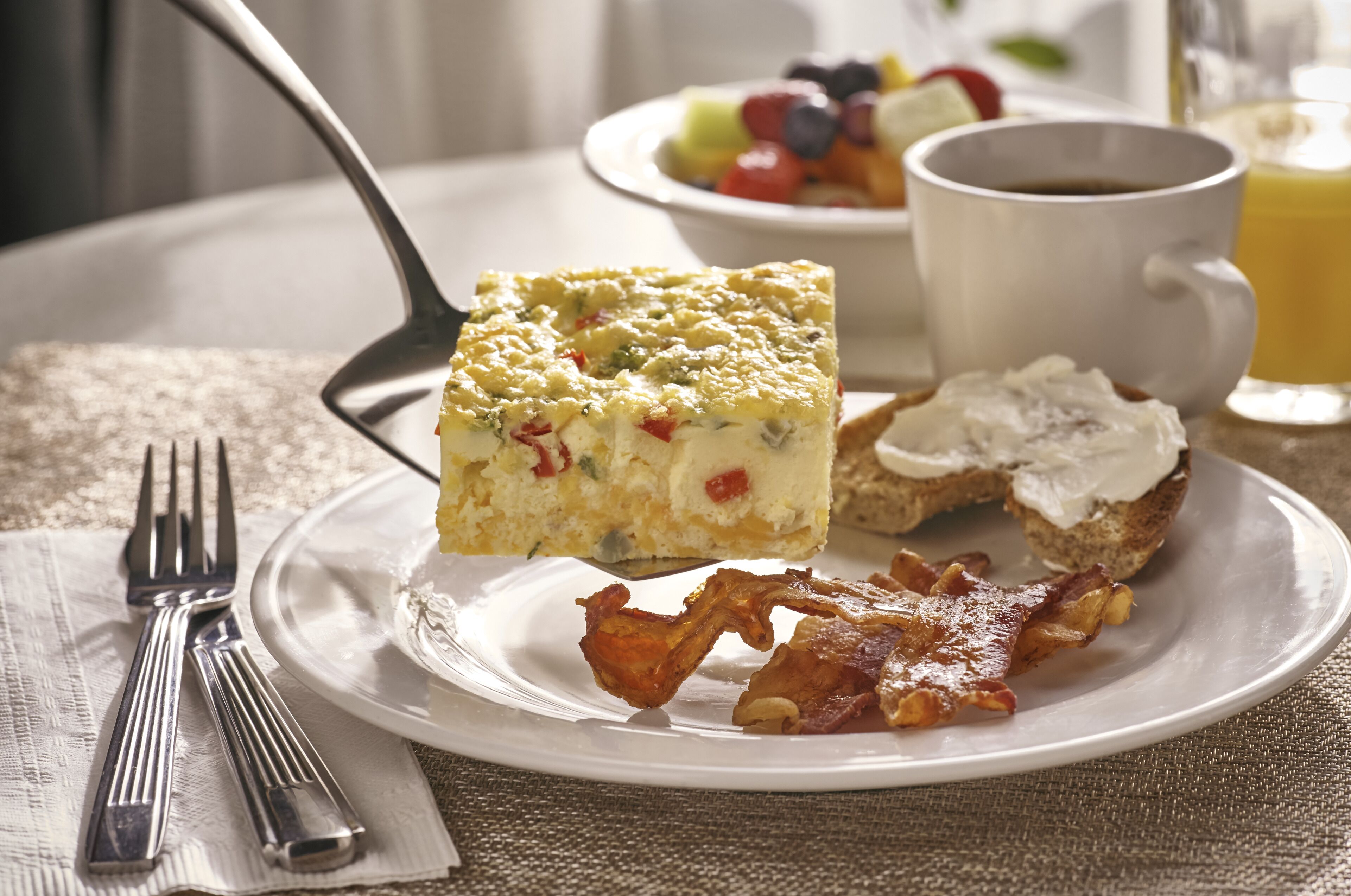 A breakfast plate with a slice of quiche, bacon, and toast.