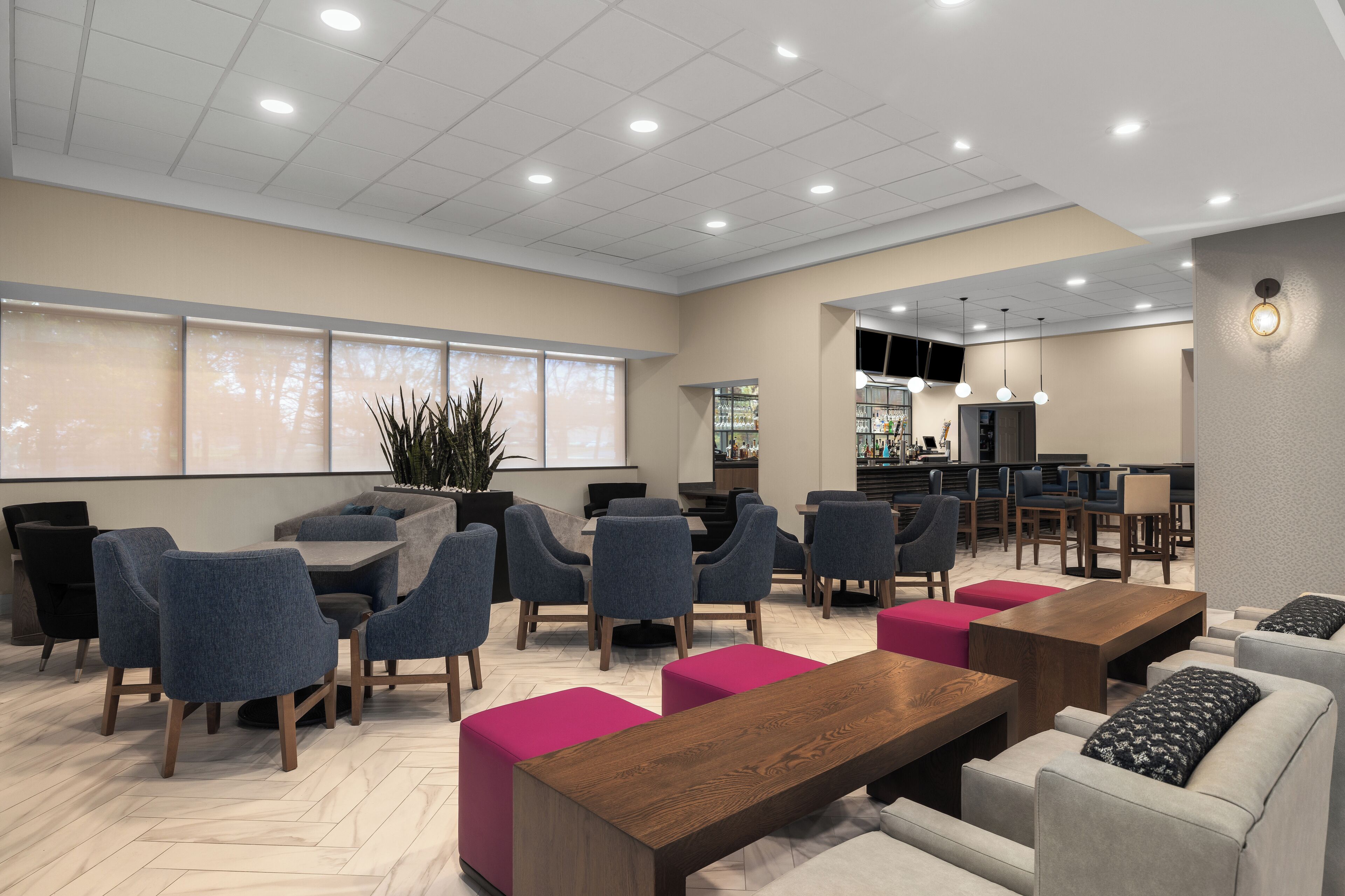 A modern lounge area with seating arrangements, a bar, and a large window providing natural light.