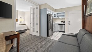 A hotel room with a kitchenette, a gray sofa, a small table, and a TV.