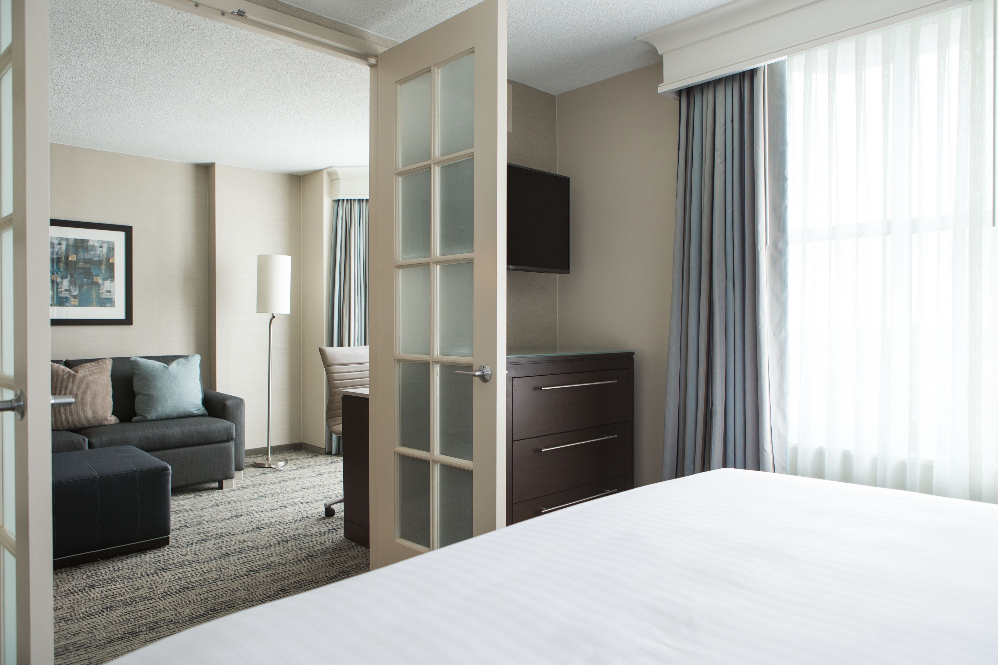 Une chambre d’hôtel comprenant un lit, une commode, un téléviseur, un canapé et une porte donnant sur une autre pièce.