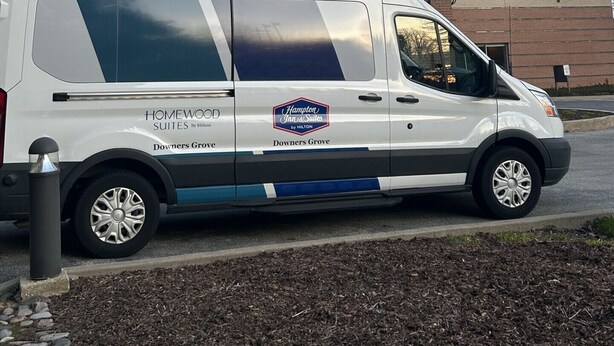 Een witte bestelwagen geparkeerd voor een gebouw met een bakstenen gevel en grote ramen.