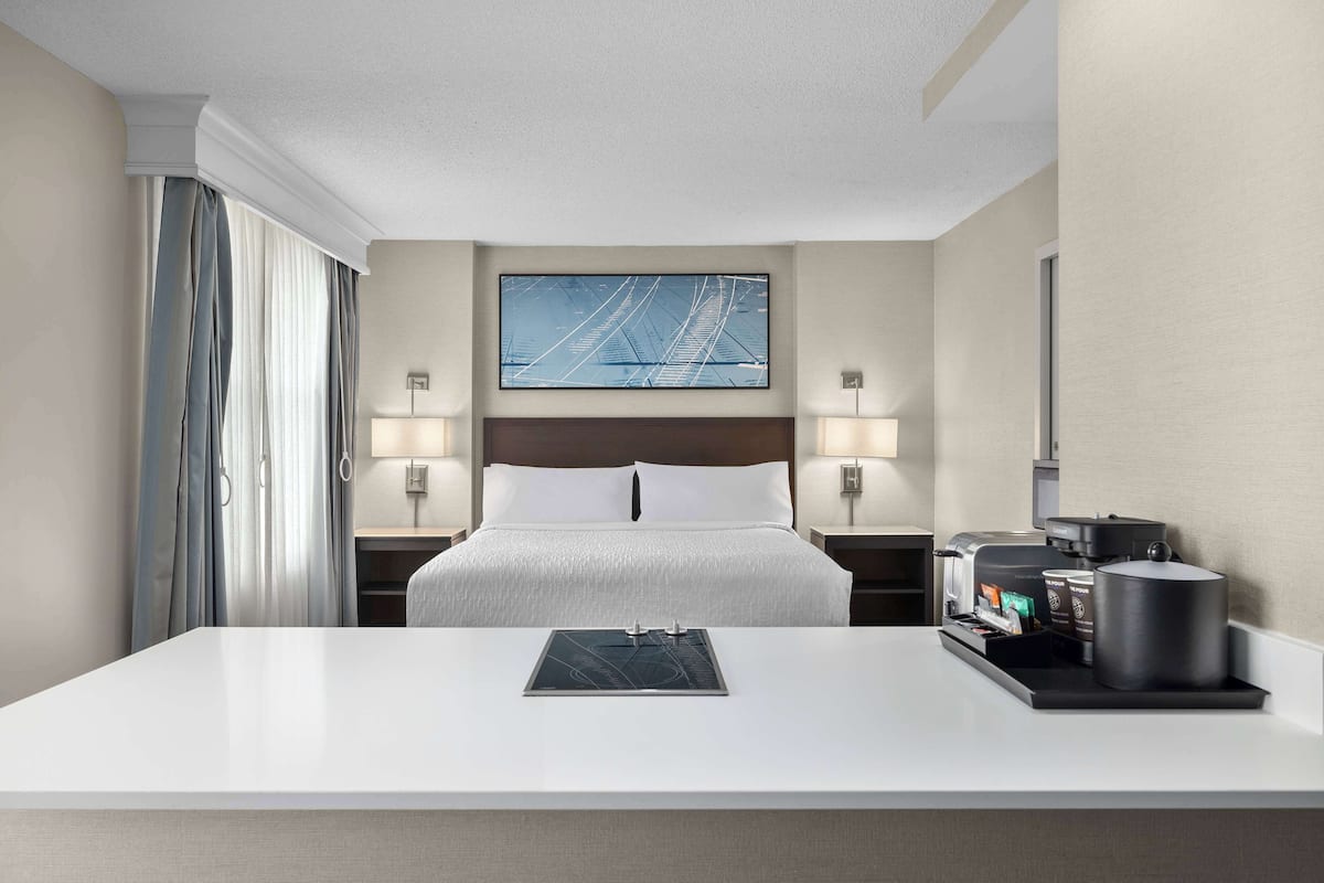 Ein Hotelzimmer mit Bett, Nachttischlampen, einer Kaffeemaschine und einer Frühstückstheke.