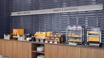 Zona de desayuno de hotel con un mostrador que exhibe diferentes alimentos y una máquina de café.