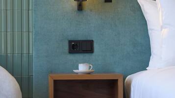 A hotel room with a bed, a nightstand with a lamp, and a small table with a cup.