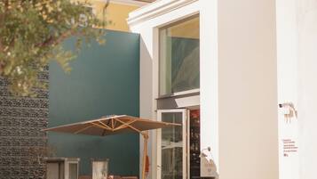 Un espace extérieur moderne aménagé avec des tables et des chaises, une entrée avec une porte vitrée et un mur en pierre.