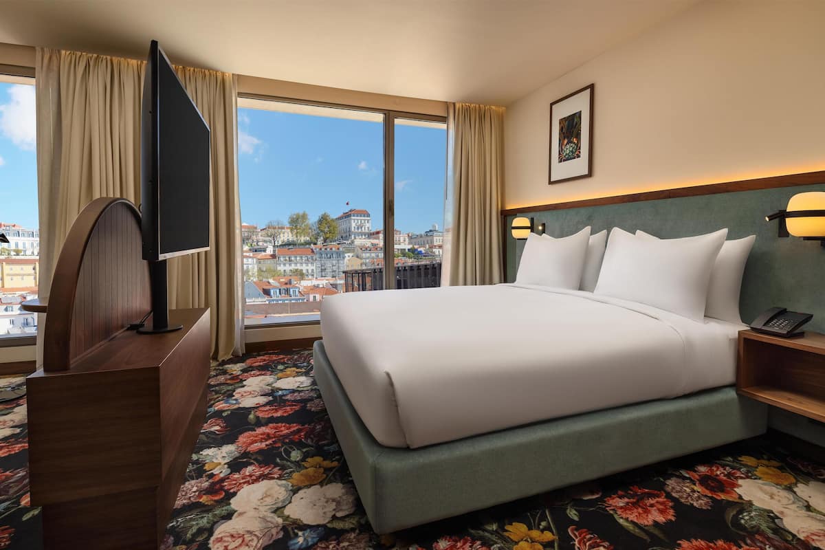Une chambre d’hôtel avec un grand lit, une télévision, un bureau et une vue sur la ville.