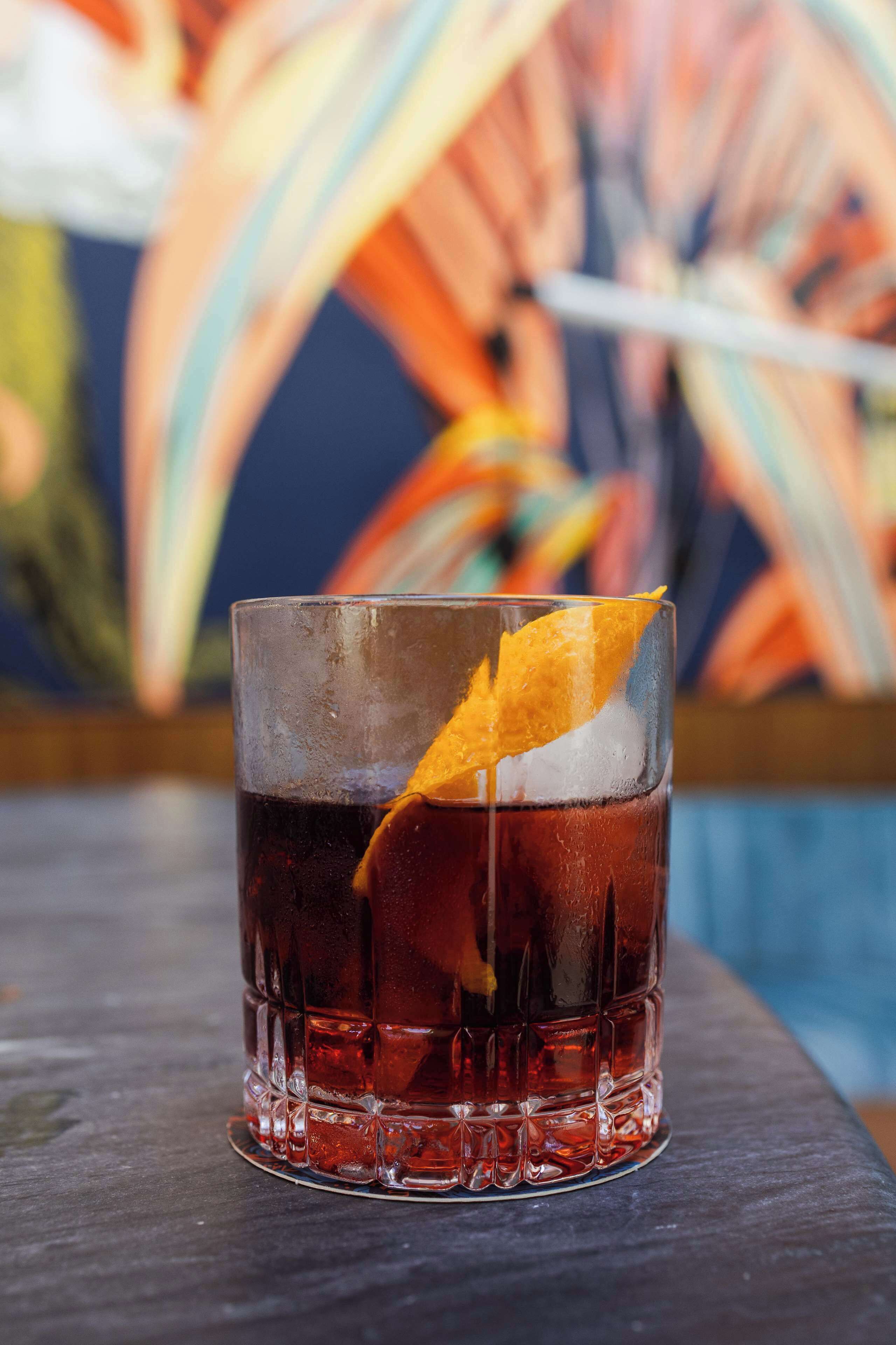 A glass of dark-colored beverage with ice and a citrus garnish on a wooden surface.