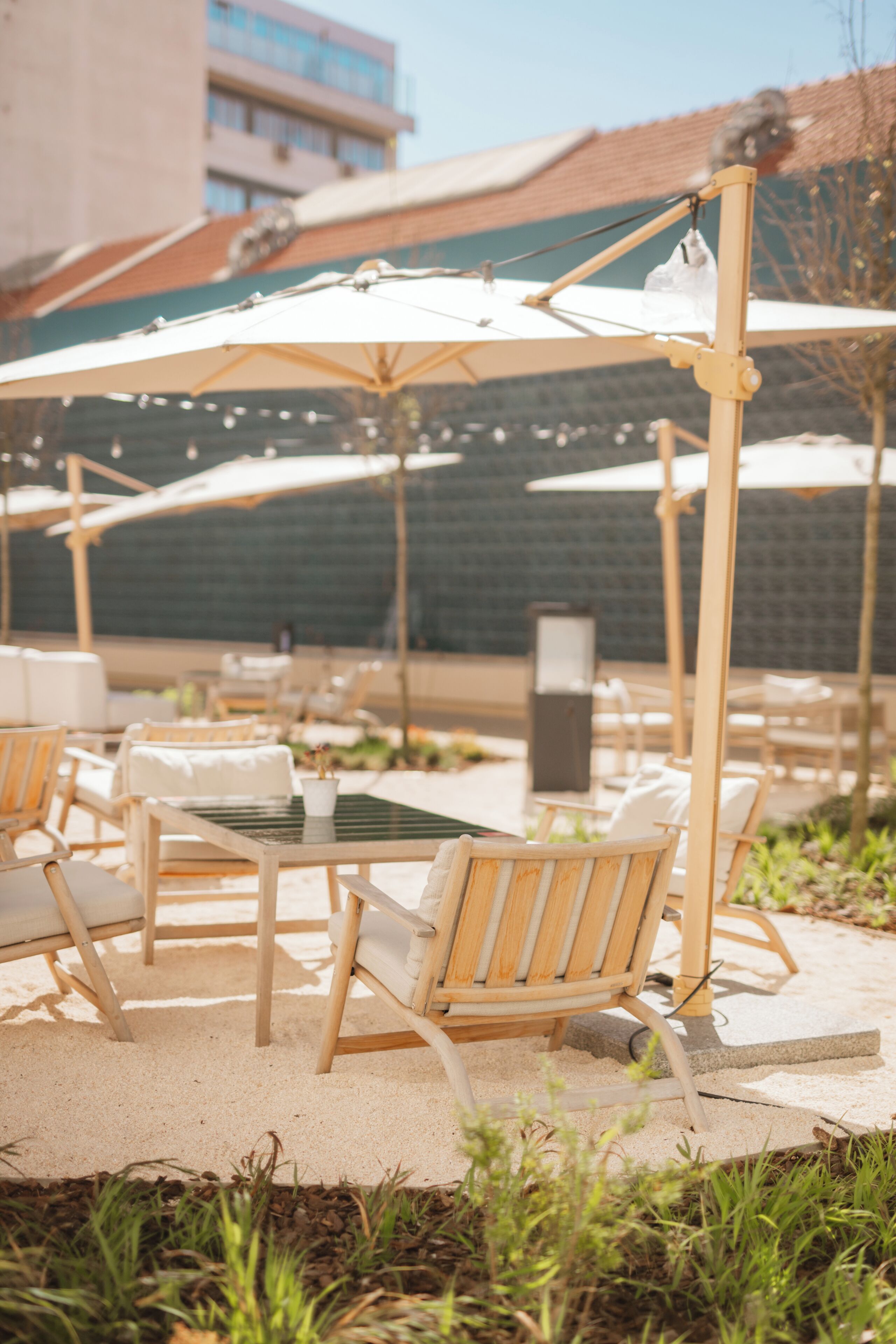Outdoor seating with umbrellas and chairs, a building in the background, and a sandy ground.