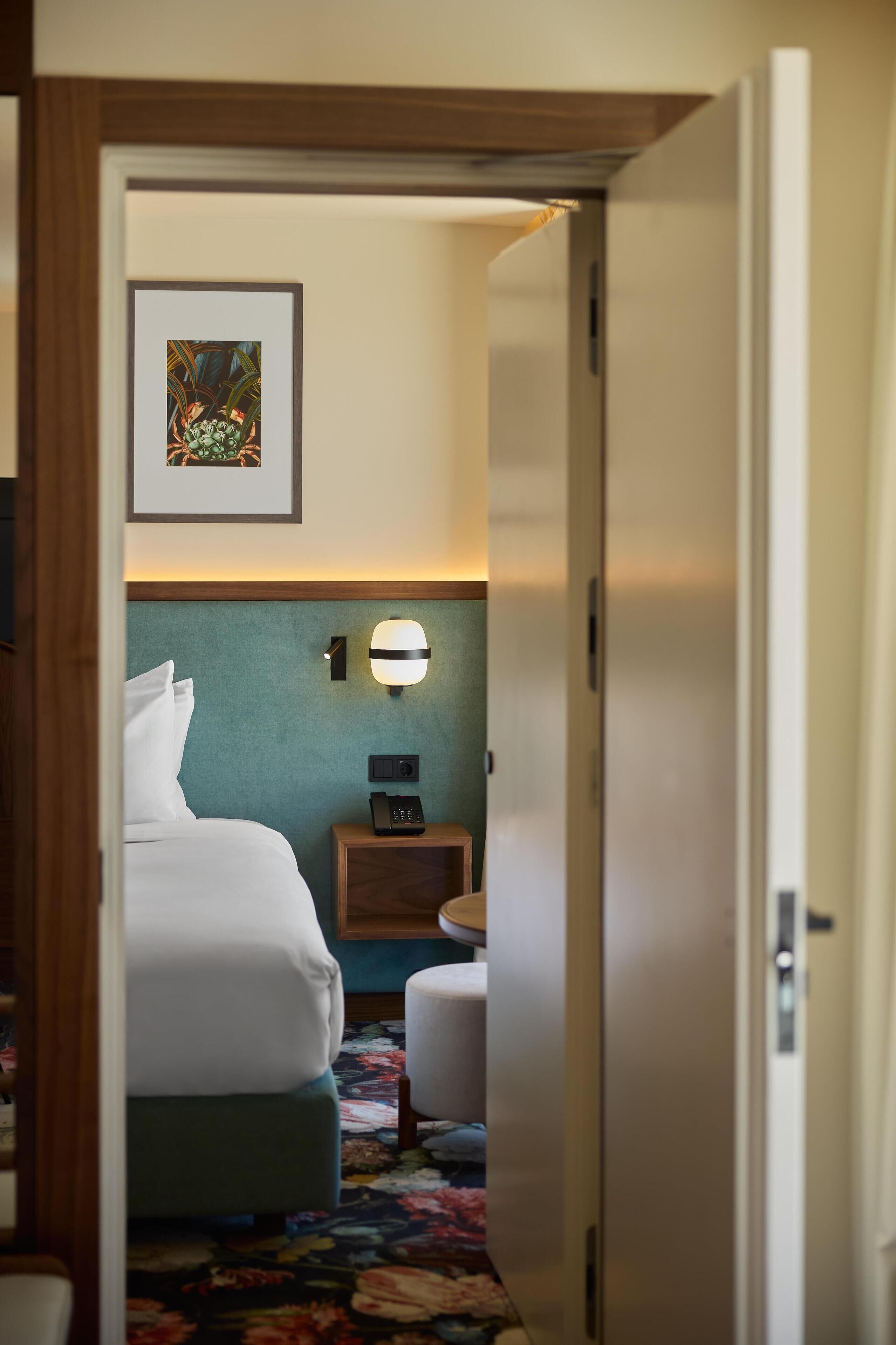 Une chambre d’hôtel avec un lit, une table de chevet avec un téléphone, une lampe fixée au mur et un tableau encadré accroché au mur.