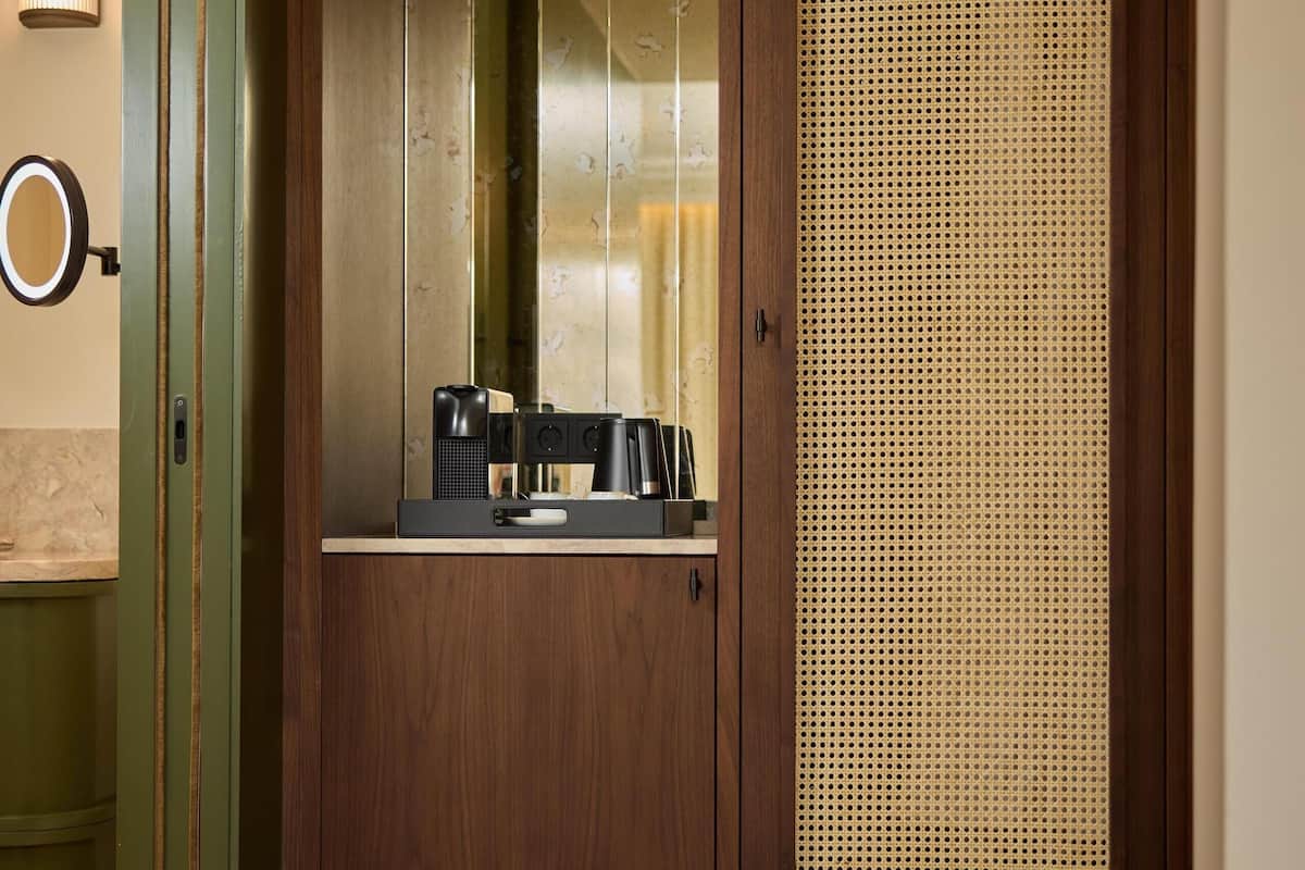 Une armoire en bois avec un miroir, un petit plan de travail avec une machine à café et un panneau de ventilation.