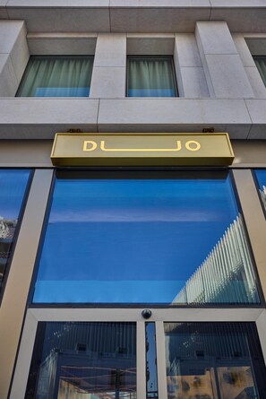 A building with a large glass facade, a sign with the name "DLJO" above the entrance, and a security camera on the lower right.