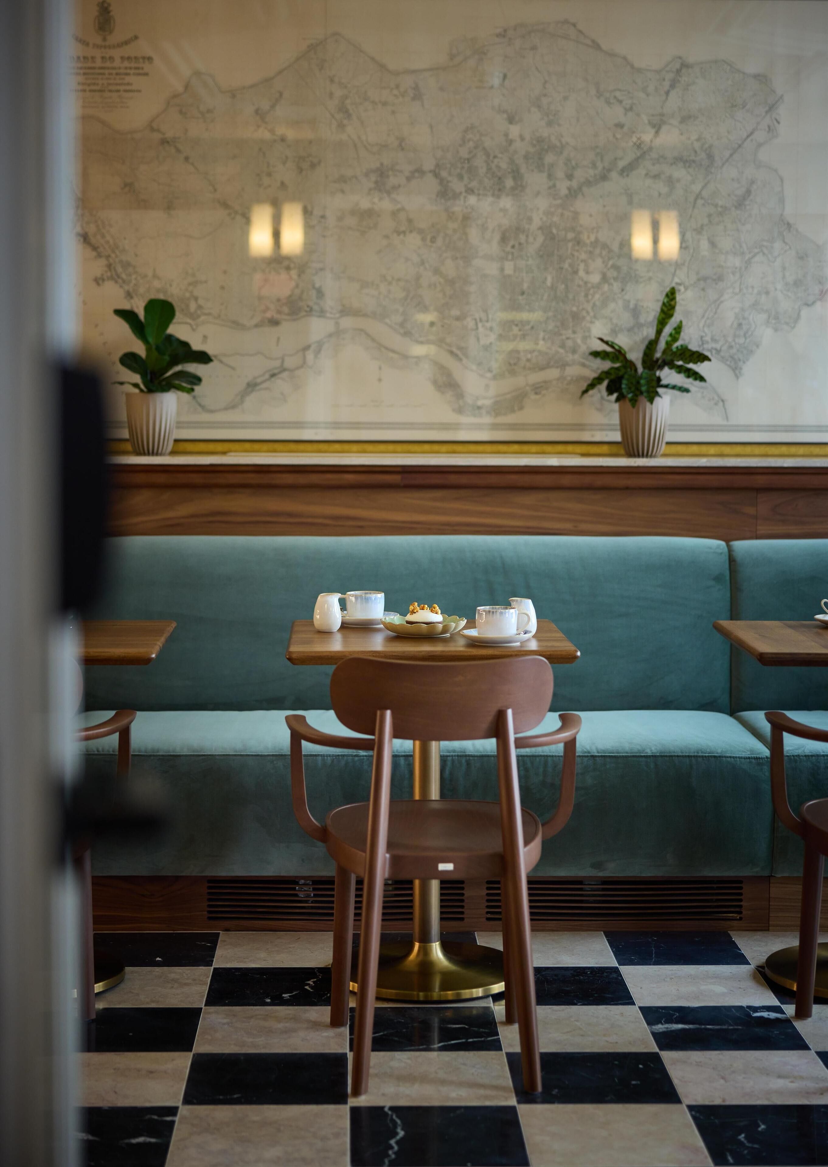 A restaurant interior with a green cushioned bench, a round table with a white cup and saucer, and a map on the wall.