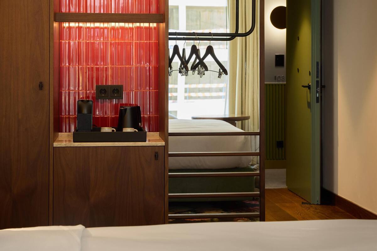 Une chambre d’hôtel avec une armoire en bois, un lit, une table de chevet avec une machine à café et une vue sur la ville par la fenêtre.
