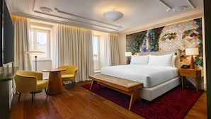 Ein Hotelzimmer mit einem großen Bett, einem kleinen Tisch, einem Sessel und einem Fernseher.