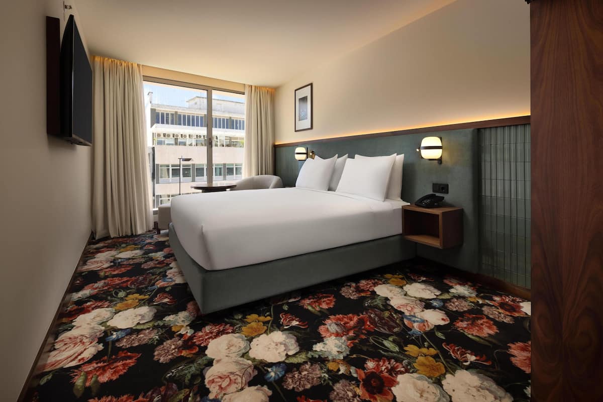Une chambre d’hôtel avec un grand lit, un bureau, une chaise, une télévision et une fenêtre avec des rideaux.