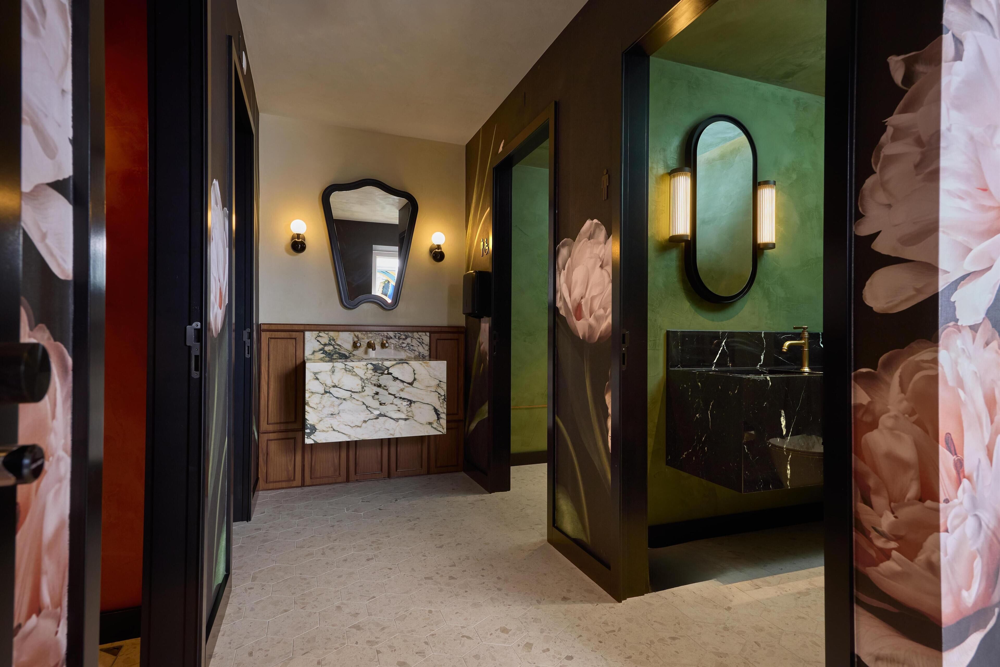 Un pasillo con un tocador de mármol, un espejo y una pared verde con diseño floral.