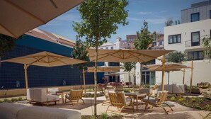 Ein Terrassenbereich im Freien mit verschiedenen Sitzgelegenheiten, darunter Sofas und Stühle, unter großen Sonnenschirmen.