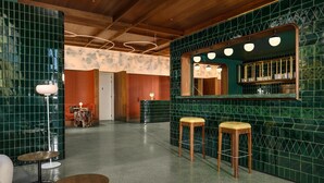 Eine Barbereich mit grünen Fliesenwänden, Holzhockern und einem Spiegel über der Bar.